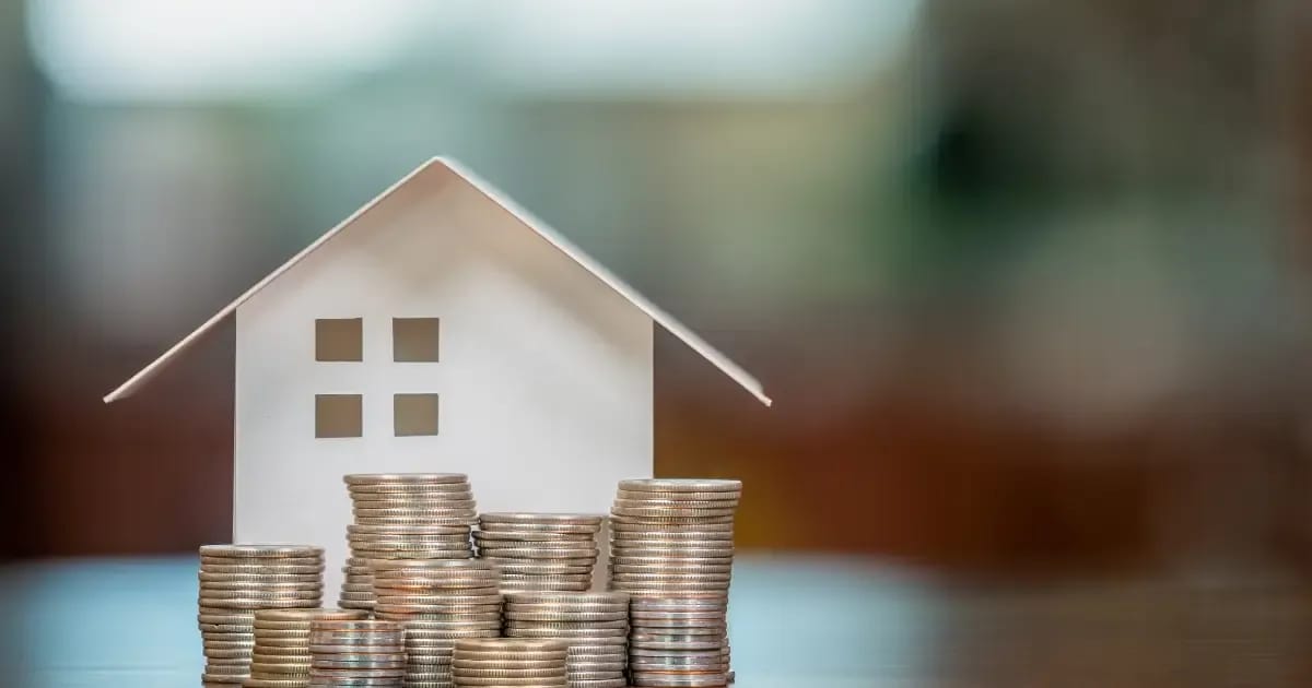 Small model of a home in need of a roof replacement with coins stacked in front of it