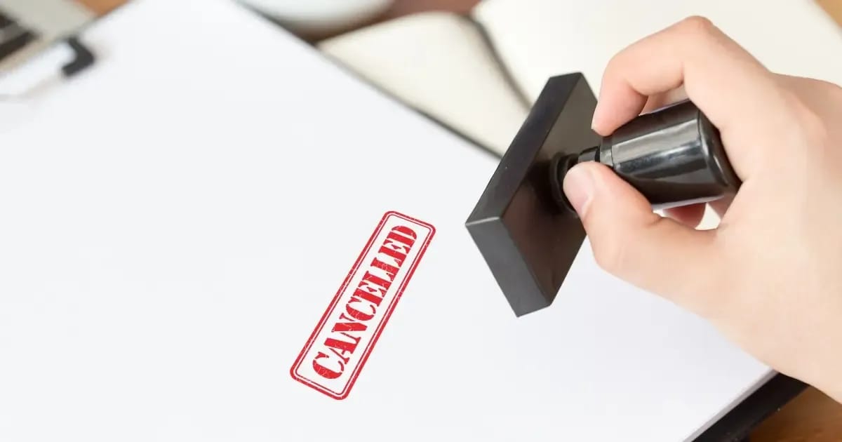 Hand stamping a homeowner's insurance policy document with the word "cancelled" due to roof condition